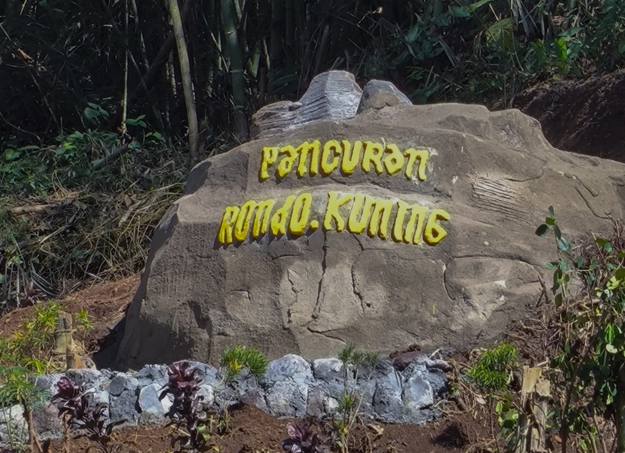 Ilustrasi Pancuran Mbok Rondo Kuning dengan air jernih mengalir di antara bebatuan dan pepohonan hijau